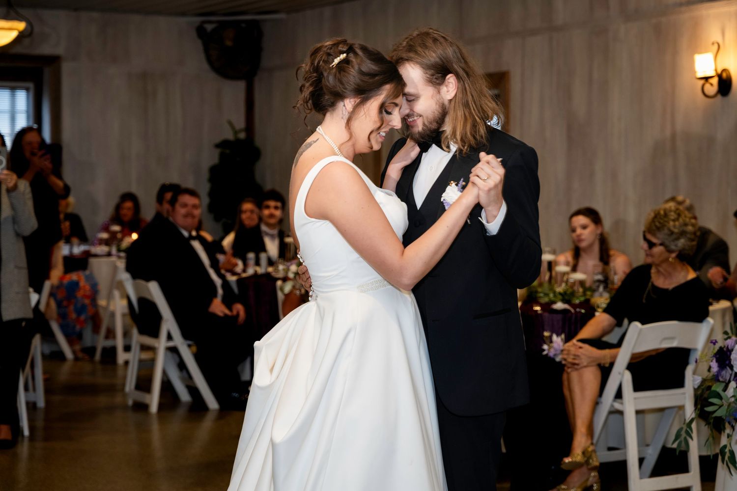 Newlyweds smiling through their first dance beneath warm reception string lights.