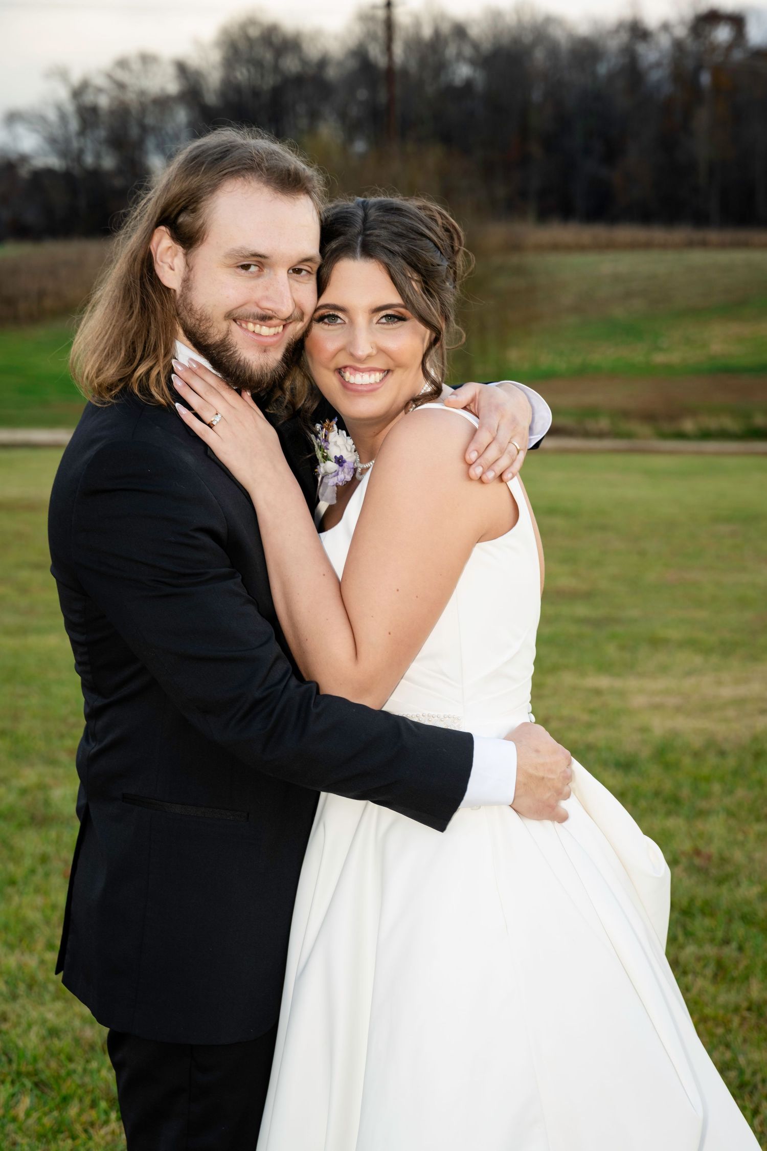 Bride and groom embracing in soft golden-hour light on a green farm lawn.