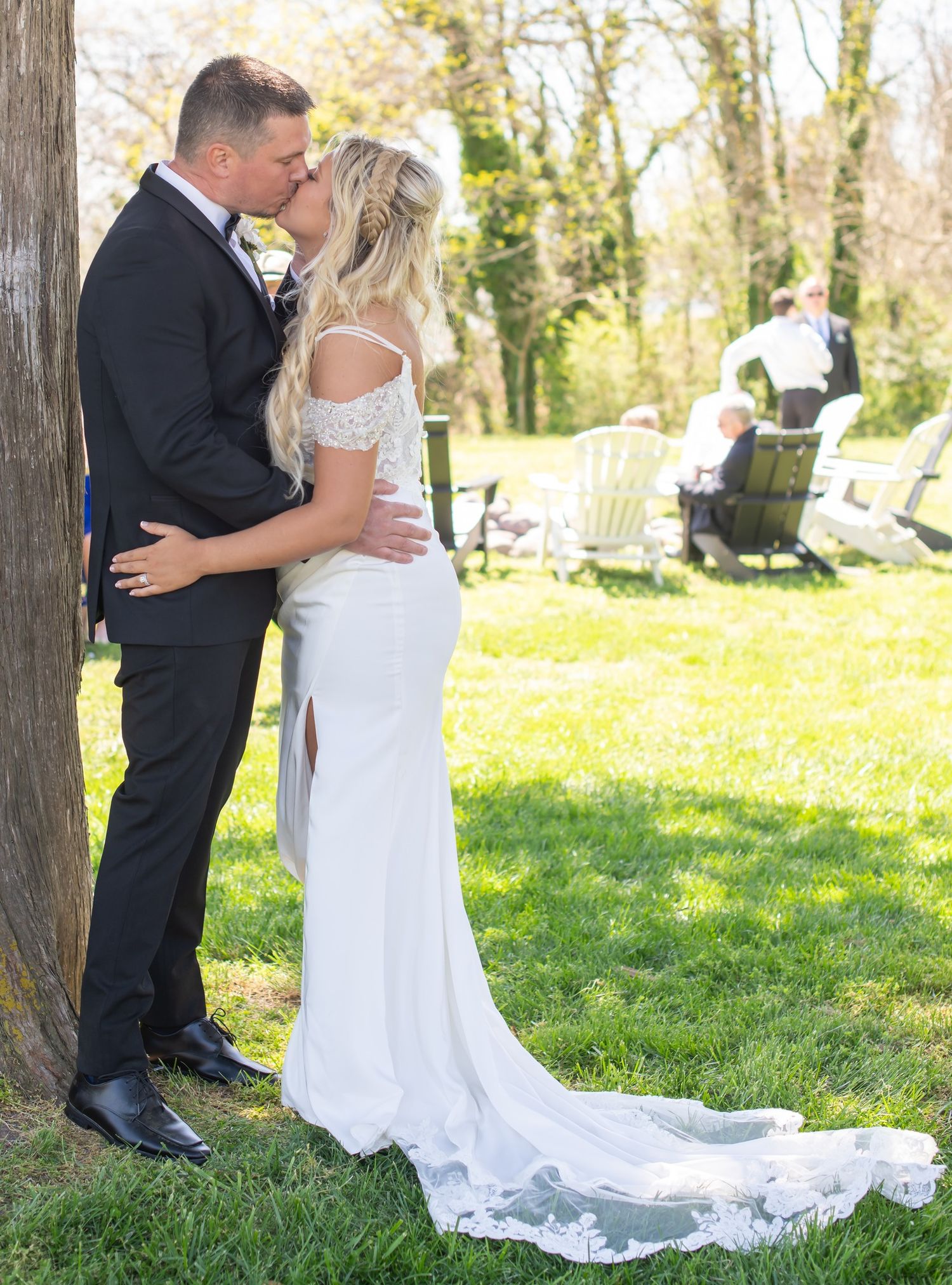 Bride and groom kissing beside a tree during sunny garden wedding portraits.