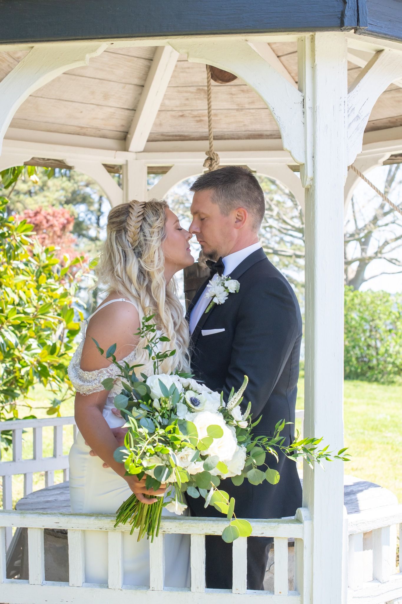 Bride and groom sharing a tender kiss inside a white garden gazebo.