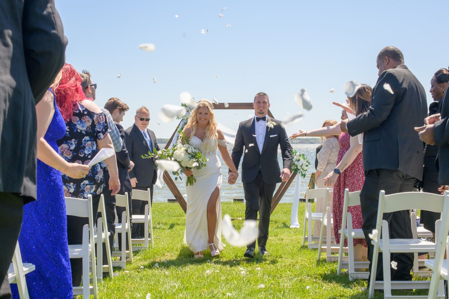 Newlyweds walking back down the aisle while guests toss white flower petals.