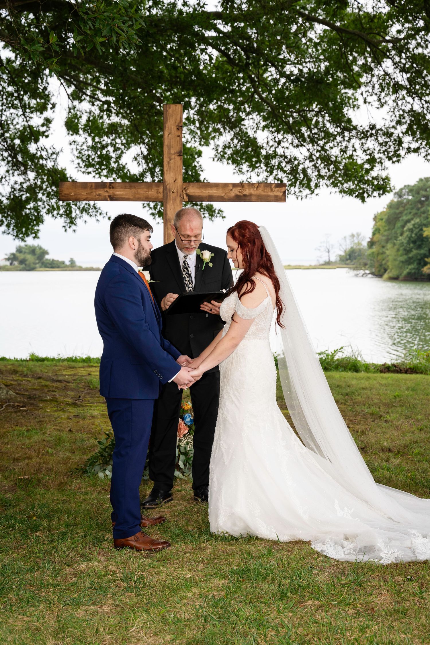 Bride and groom holding hands during their outdoor wedding vows beside a peaceful lake.
