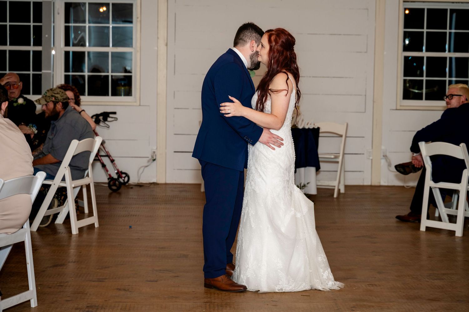 Newlyweds sharing their first dance while family and friends watch from the reception tables.
