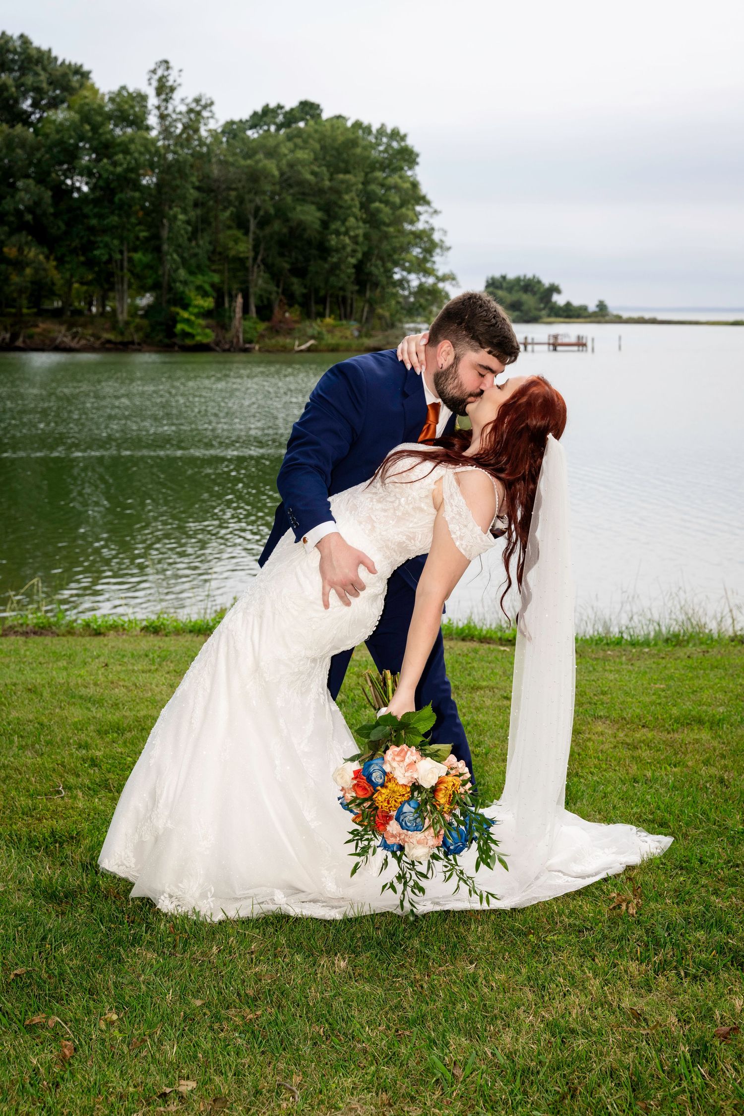 Groom dipping his bride for a kiss during romantic lakeside wedding portraits.