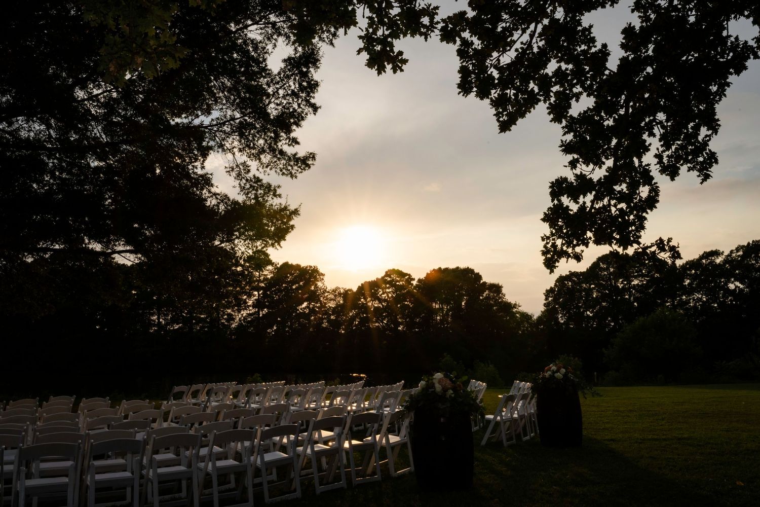 Warm sunset light falling across rows of white chairs after an outdoor wedding ceremony.