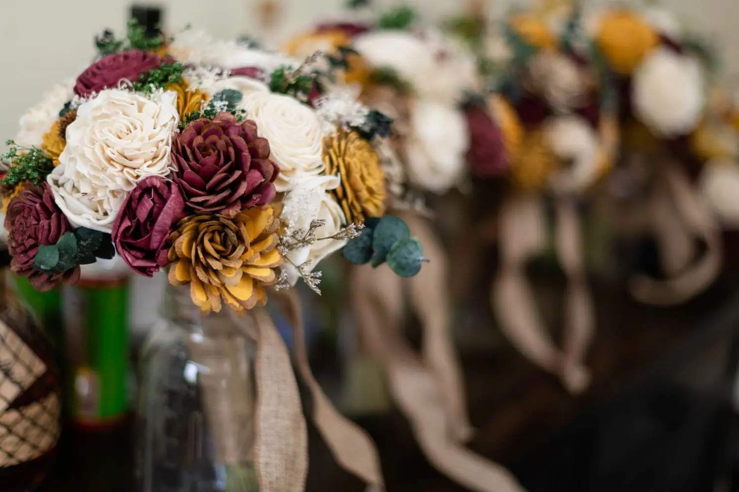 Rustic wedding bouquets with burgundy, mustard, blush, and cream flowers arranged in mason jars.