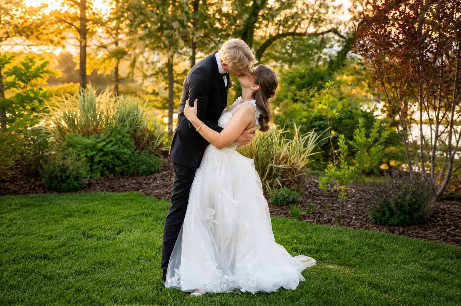 Bride and groom sharing a kiss in a colorful garden during soft golden-hour light.