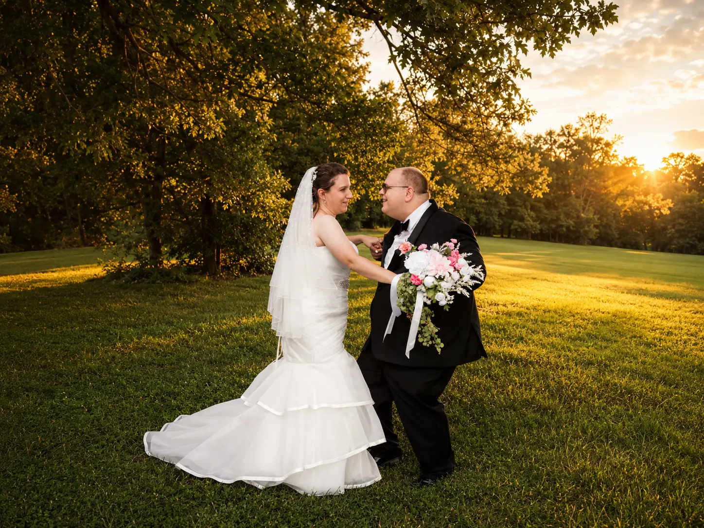 Bride and groom sharing a private dance on the lawn during a glowing golden-hour sunset.